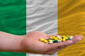 man holding capsules in front of complete wavy national flag of ireland symbolizing health, medicine, cure, vitamines and healthy life