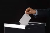 Man putting his vote into ballot box on black background, closeu