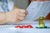 Hand of senior woman holding leaflet to prescribed medicine, pills lying beside on table. Closeup patient reading information sheet. Concept of healthcare