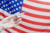 Doctor's hand holding syringe with vaccine over United States of America flag background. USA Vaccination.