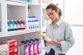 Young woman customer holding sunscreen bottles at pharmacy