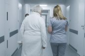 Female doctor, nurse with digital tablet walks along the clinic corridor with elderly woman, helps patient to get to hospital ward after procedures. Medical staff, patients in medical center hallway.