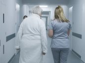 Female doctor, nurse with digital tablet walks along the clinic corridor with elderly woman, helps patient to get to hospital ward after procedures. Medical staff, patients in medical center hallway.