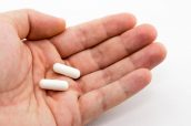 A closeup shot of a person holding two white capsules with a white background